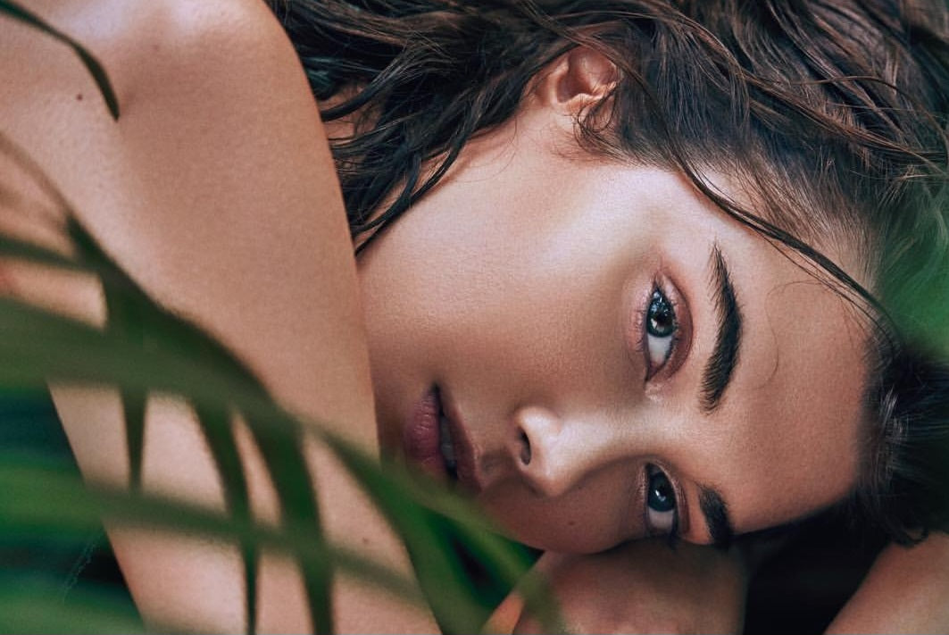 Woman with glowing skin among green leaves, simple skincare routine guide by LUME