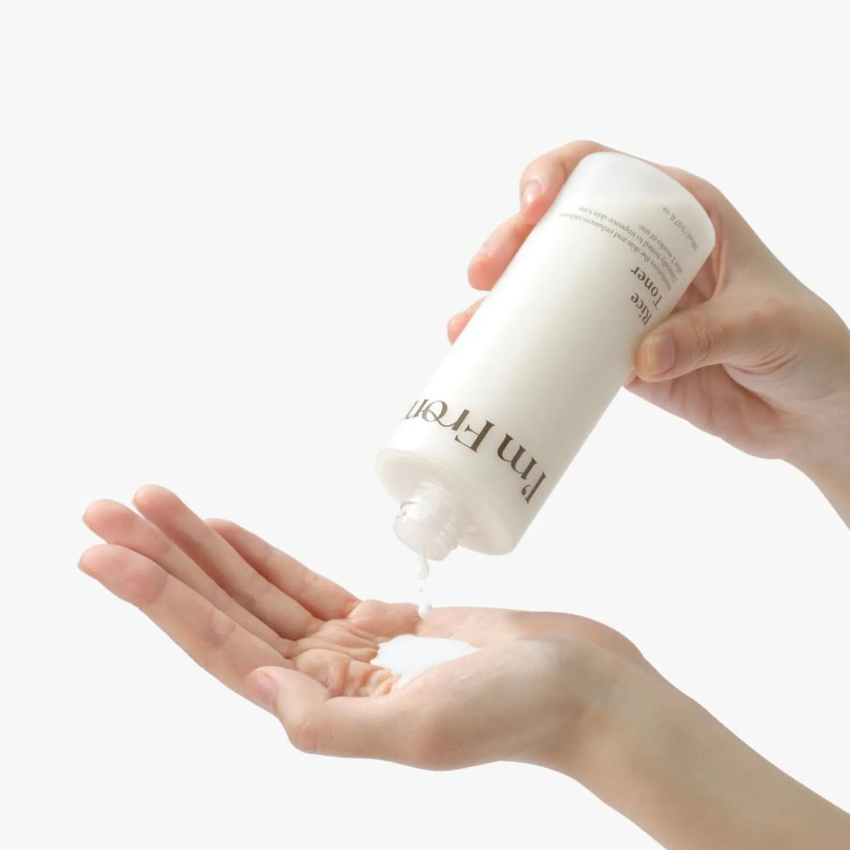 Person holding a white bottle labeled 'I'm from Rice Toner' over their palm on a light background, Hydrating Korean toner for balanced skin, LUME